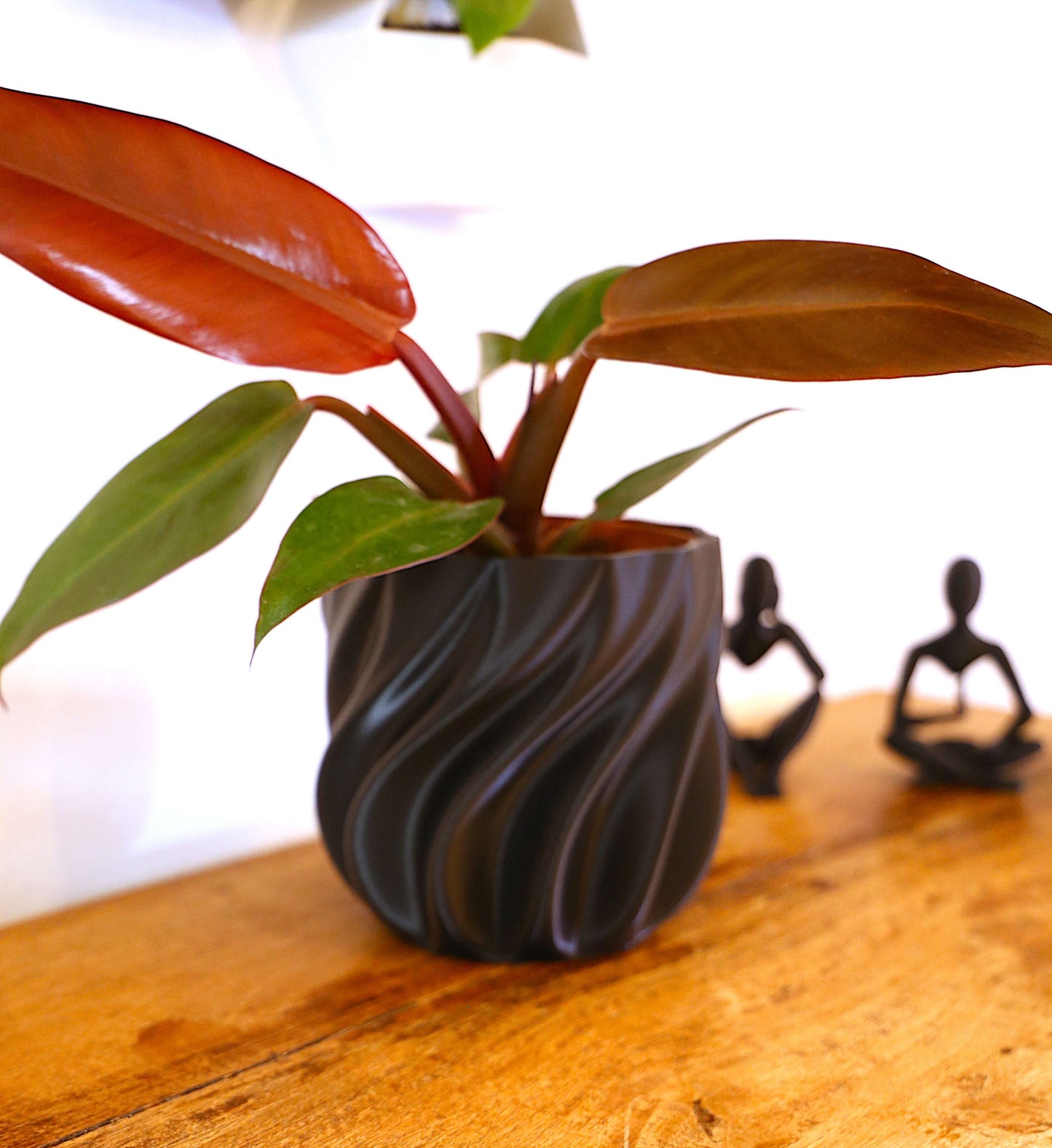 Vaso Onda in plastica con piante verdi e foglie rosse su un tavolo in legno, decorazione moderna per interni.